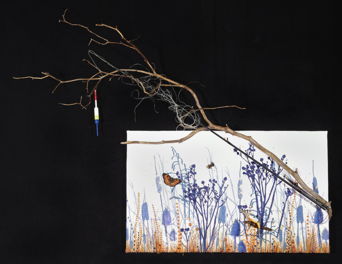 A branch with a fishing bobber in front of a quilt with butterflies and tall grass
